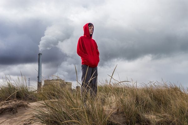 Teenage boy stands looking ahead with power plant fumes behind him