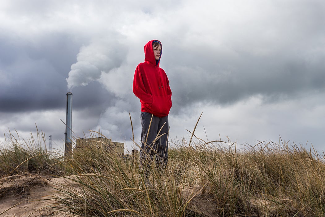 Teenage boy stands looking ahead with power plant fumes behind him