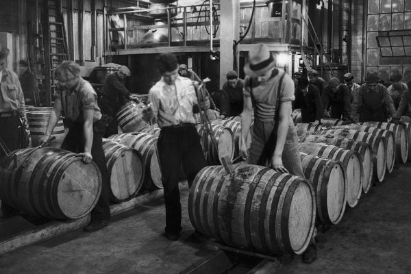 Barrels of whiskey are opened and poured into a blending vat below, circa 1940.