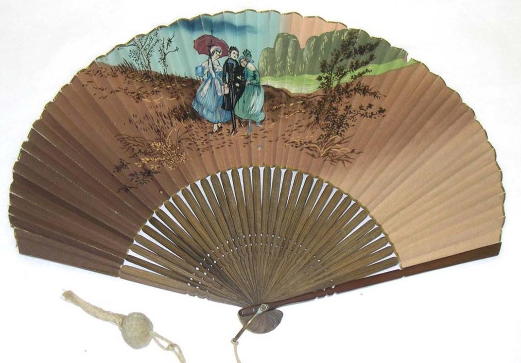 Fan with wooden sticks and guards. Paper leaf is painted with a scene of two women and one man in Western dress in a mountain setting. A tassel is attached to the handle.