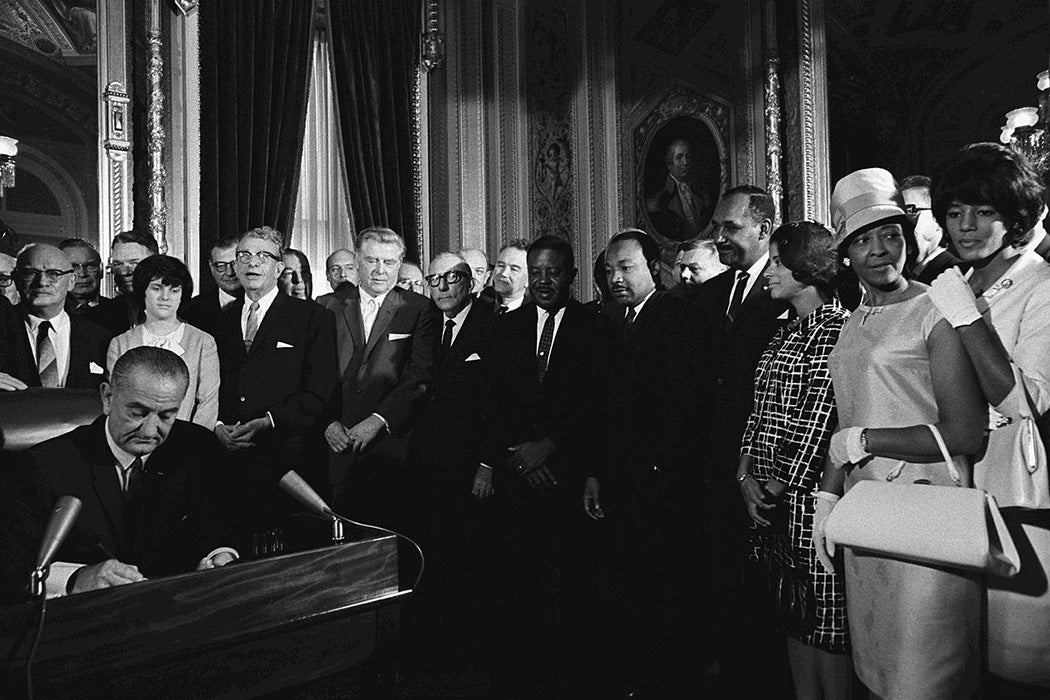 President Lyndon B. Johnson signs the Voting Rights Act of 1965 while Martin Luther King and others look on