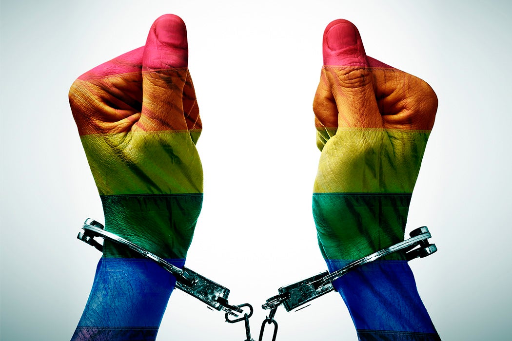 closeup of the hancduffed hands of a person patterned as the gay pride flag