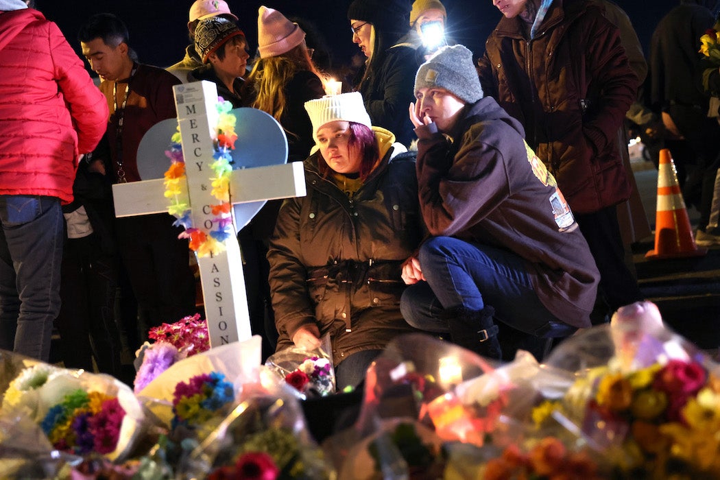 two people knee before a white cross and flowers at a makeshift memorial for the five people killed by a gunman during a mass shooting at Club Q in Colorado