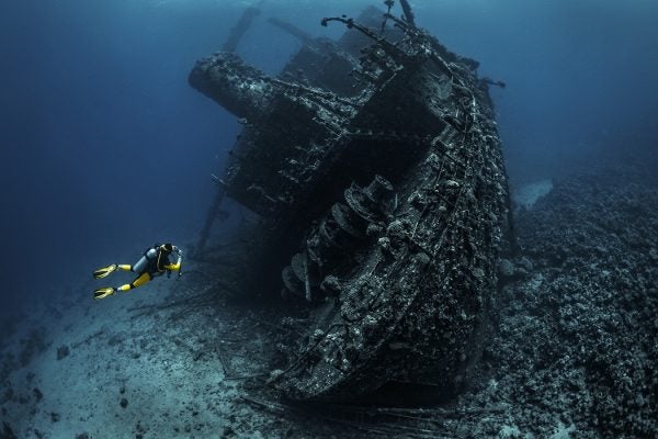 Scuba diver passing by a wreckage of a large sunken ship in the Red Sea.