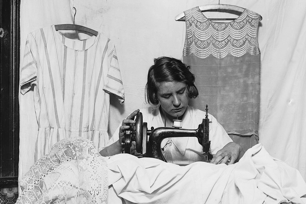 A dressmaker uses a sewing machine, 1928