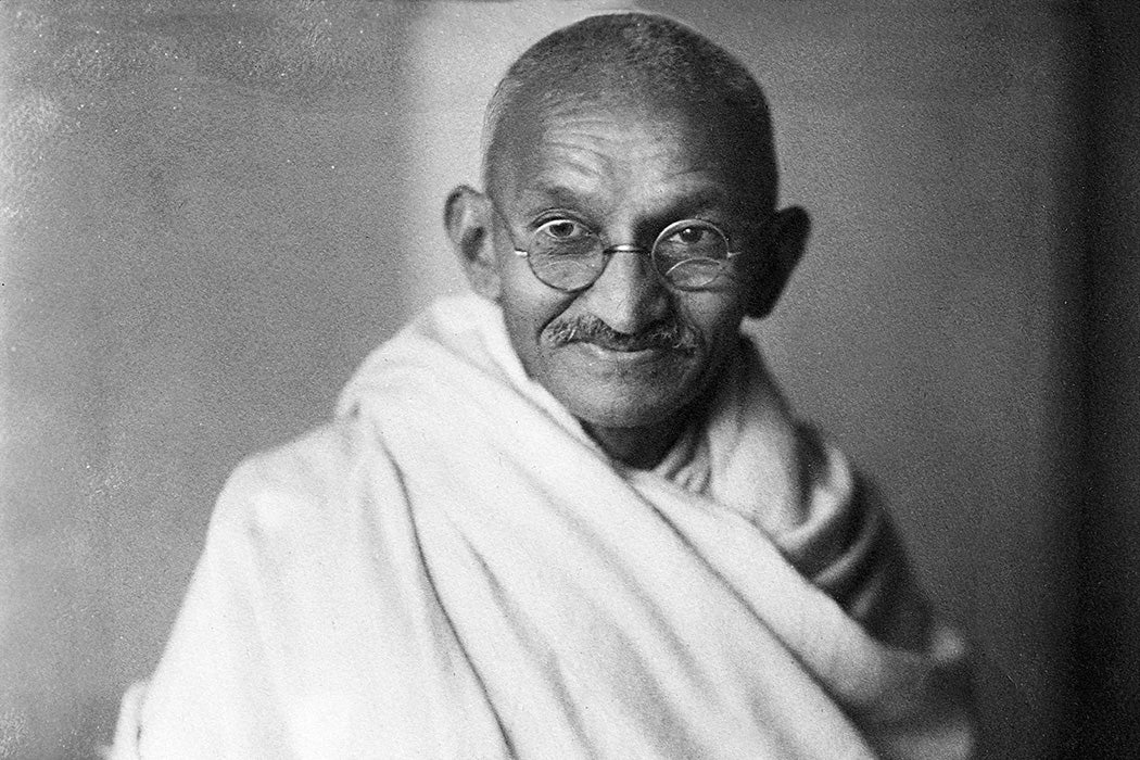 Black and white studio photograph of Mahatma Gandhi wearing a white robe, looking directly at the camera and gently smiling, London, 1931