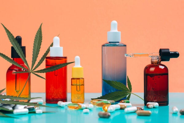 Set of CBD oils and nutritional supplements made of cannabis on orange-turquoise background with cannabis leaves. Five multicolored glass bottles placed in a row. Front view