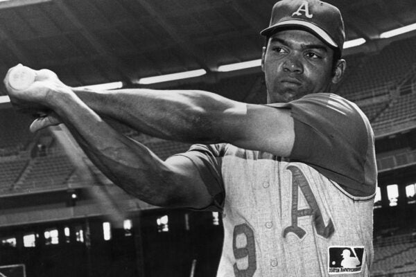 1969: American athlete Reggie Jackson of the Oakland Athletics, swinging a bat while in uniform, on the field of an empty baseball stadium.