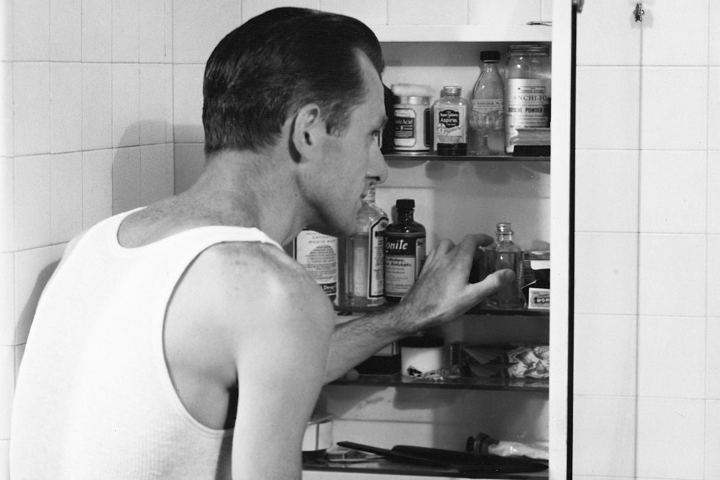 A man looks through his medicine cabinet in the bathroom, circa 1955.