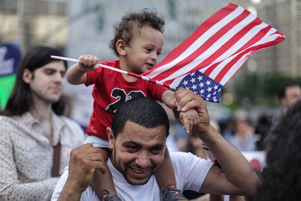 Saad Almontaser, 1, of Brooklyn, waves an American flag over his father Ali, from Yemen, as protesters hold a rally outside of Manhattan Federal Court on June 26, 2018 in New York City.