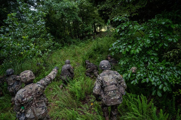 Cadets of the 3rd Regiment approach their objective as a simulated mortar shell explodes in the distance in Training Area 9 during Army ROTC Cadet Summer Training on July 1, 2021 in Fort Knox, Kentucky