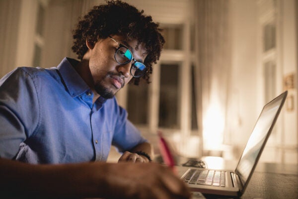 Young black student studying at night at home, with a help of a laptop computer.