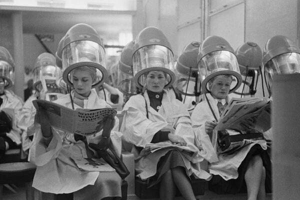 A row of British women sitting under hairdryers in a Paris salon
