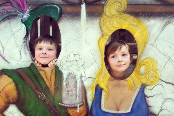 Two children posing behind a photo stand-in of Renaissance people with big mugs of beer.
