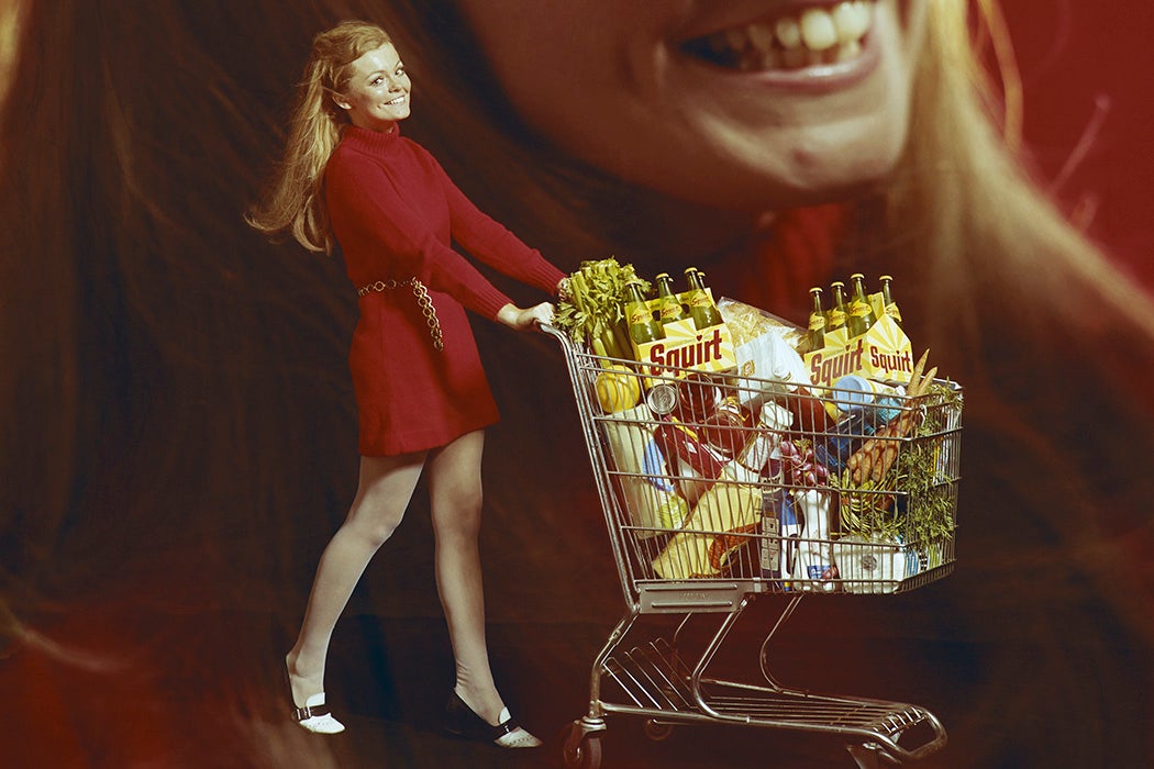 Woman pushing shopping trolley on red background, smiling, portrait