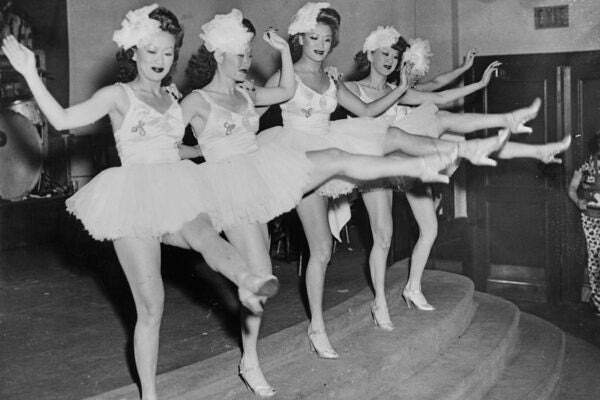 A line of five Asian American dancers, each wearing a tutu, kicking out their left legs as they perform the can-can at the Forbidden City nightclub in San Francisco, California, circa 1945.