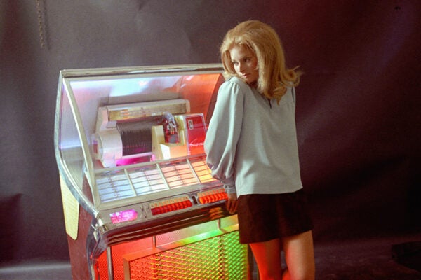 A young woman stands in the glow of a multicolored Juke box in the late 1960's.