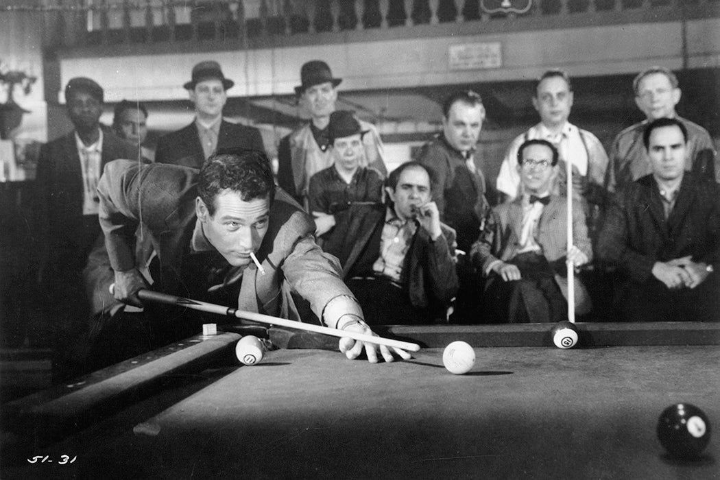 Paul Newman lets a lit cigarette hang from his mouth while lining up a pool shot in a scene from the film 'The Hustler', 1961.