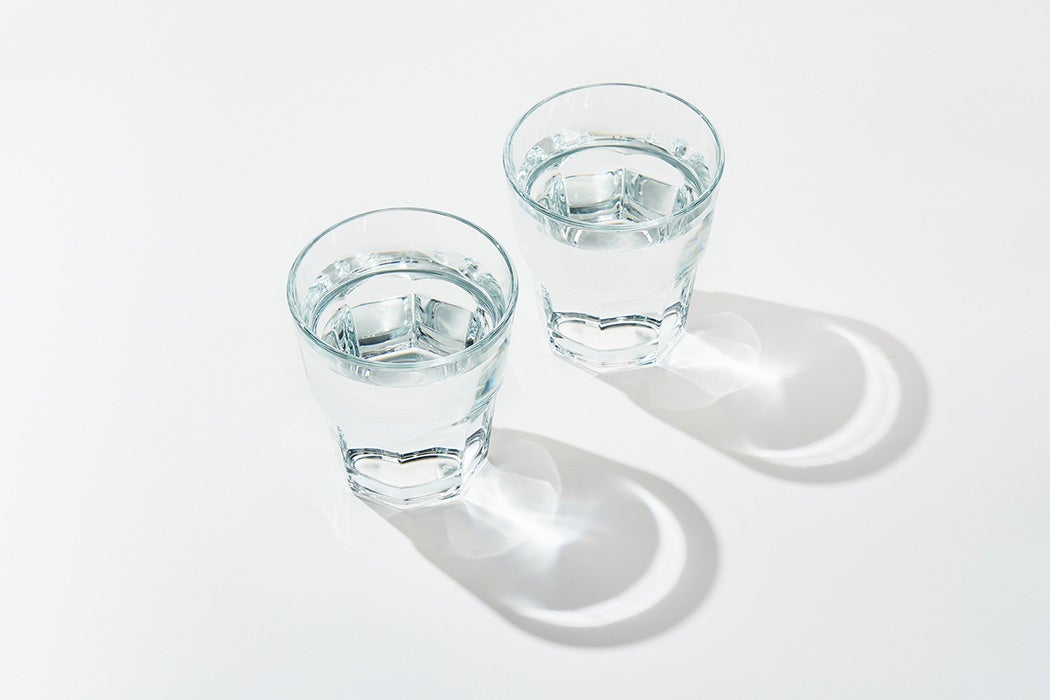 Two glass of fresh pure water on white background with sunlight deep shadow of glass.