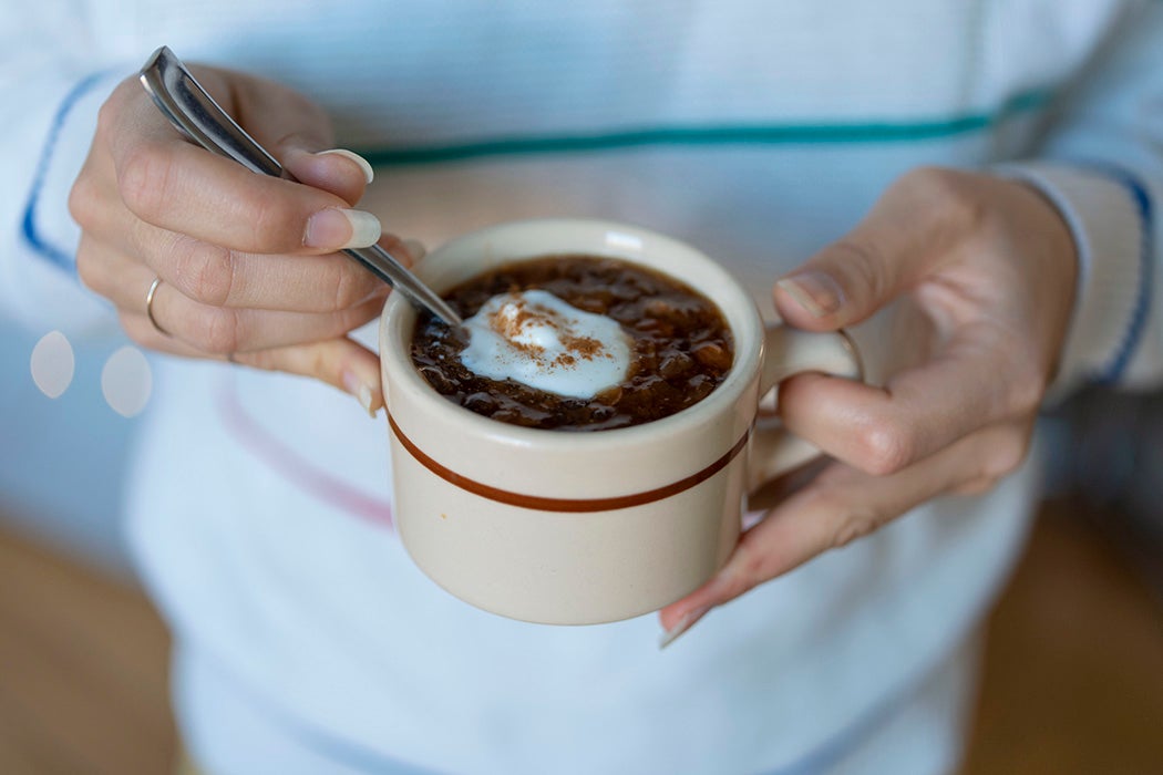 A woman's hands holding a mug of fruit soup