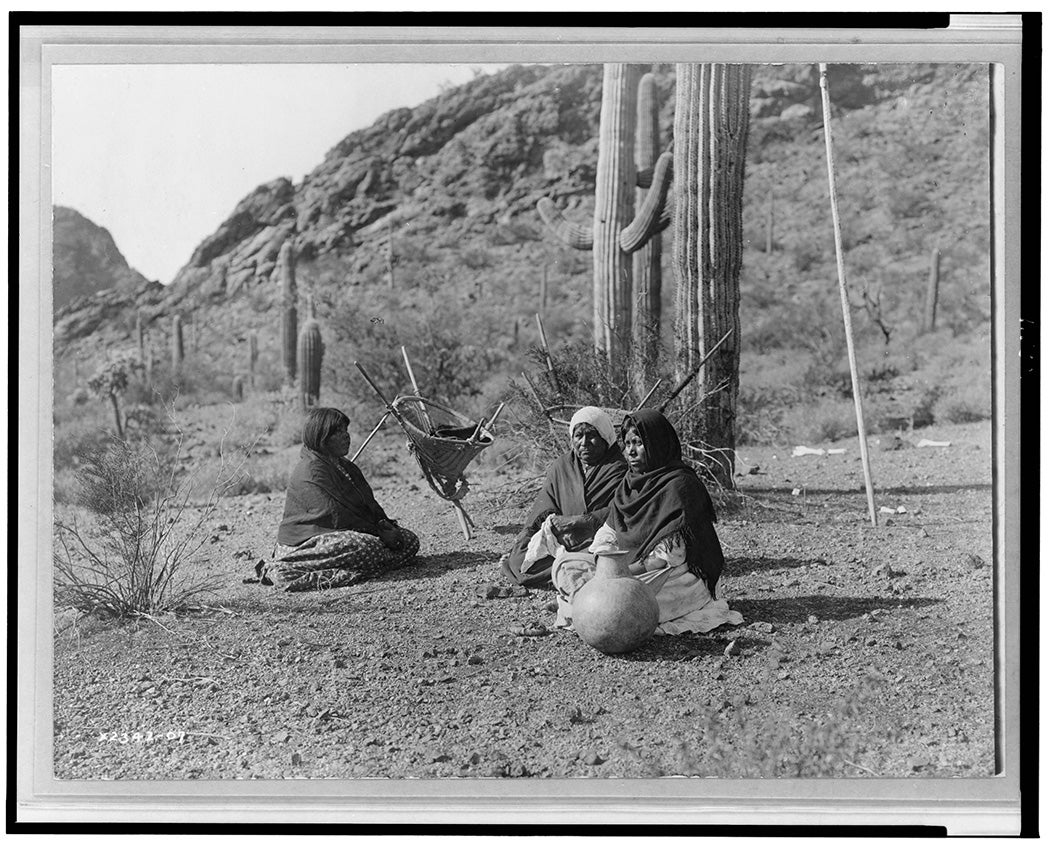 Qahatika women rest during a saguaro harvest. A kuipad stands in the background.