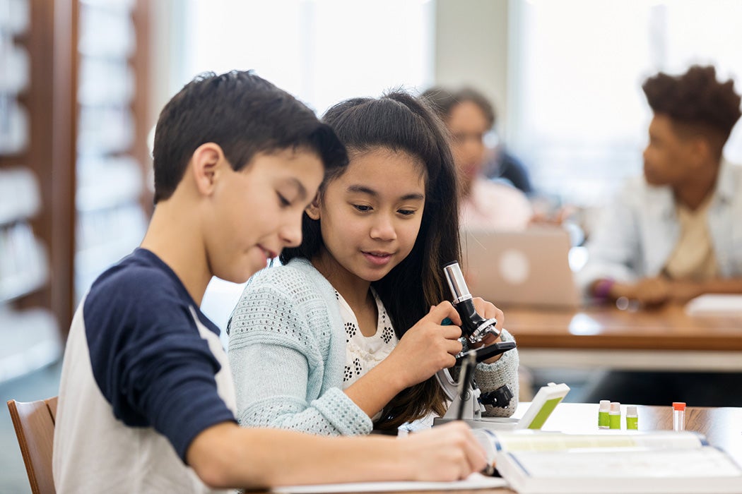 Confident students use work together on a science assignment. They are analyzing something with a microscope.