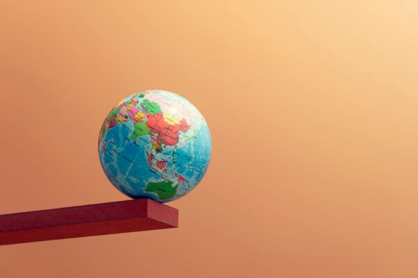 A earth globe balancing on the edge of a stick, symbolizing climate crisis