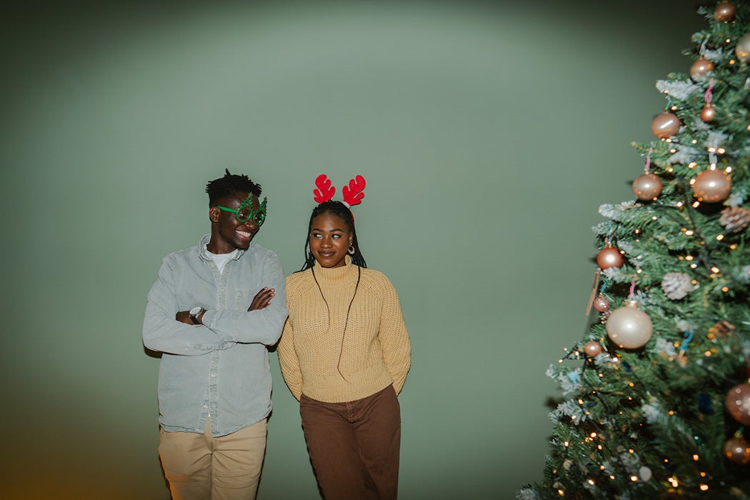 Photo of a playful couple in holiday accessories by the Christmas tree