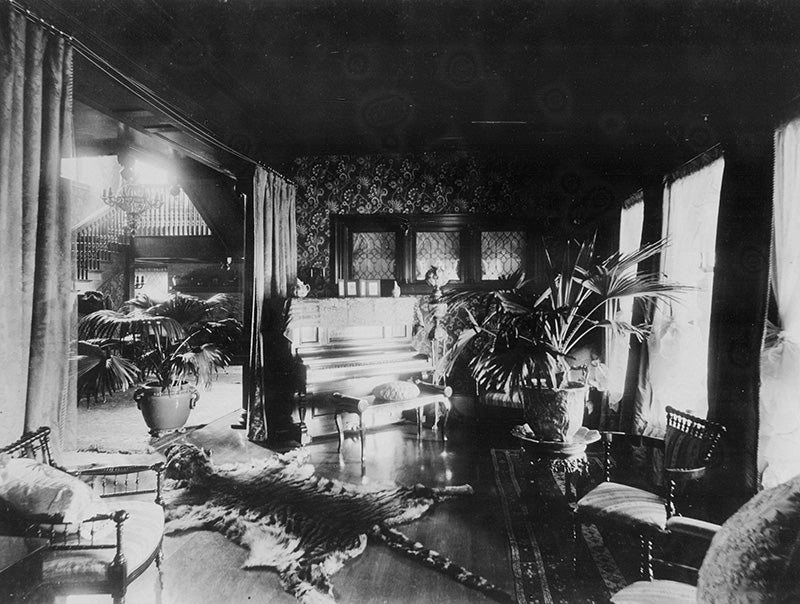 A room off the entrance hall of the Hord residence, with William Morris style wallpaper, a tiger skin rug, hanging light fixtures, and a view of the main staircase.