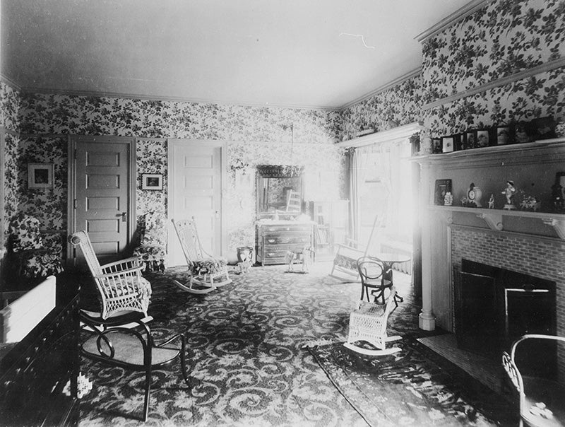 A child's room in the Hord residence with flowered wallpaper, wall to wall carpet, a tiled fireplace, a wood mantel, gas light fixtures, and a toy horse and cow.