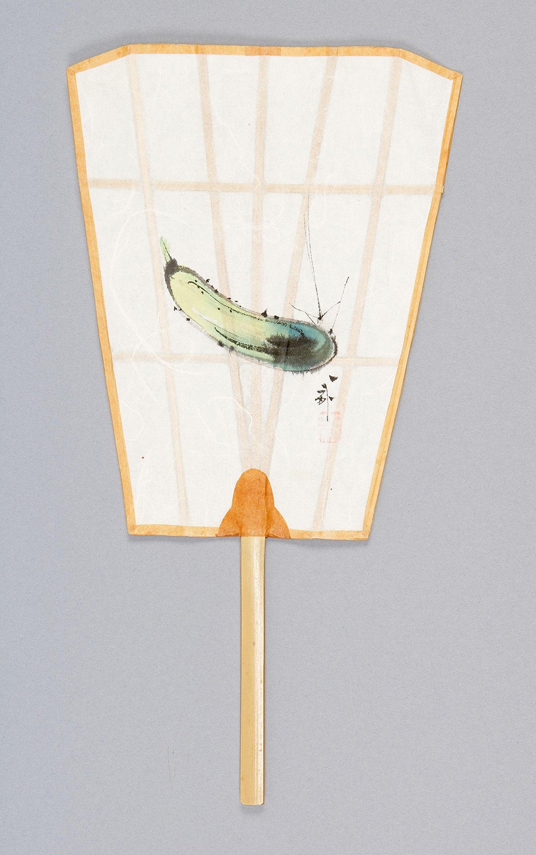 Paper hand fan with a bamboo handle, bamboo ribs, a flaring trapezoid-shape, and orange trim. One side of the fan features the image of a light green cucumber with a black character and a red stamp.