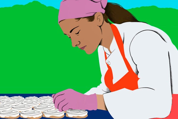 A worker carefully decorates doughnuts with white icing outside