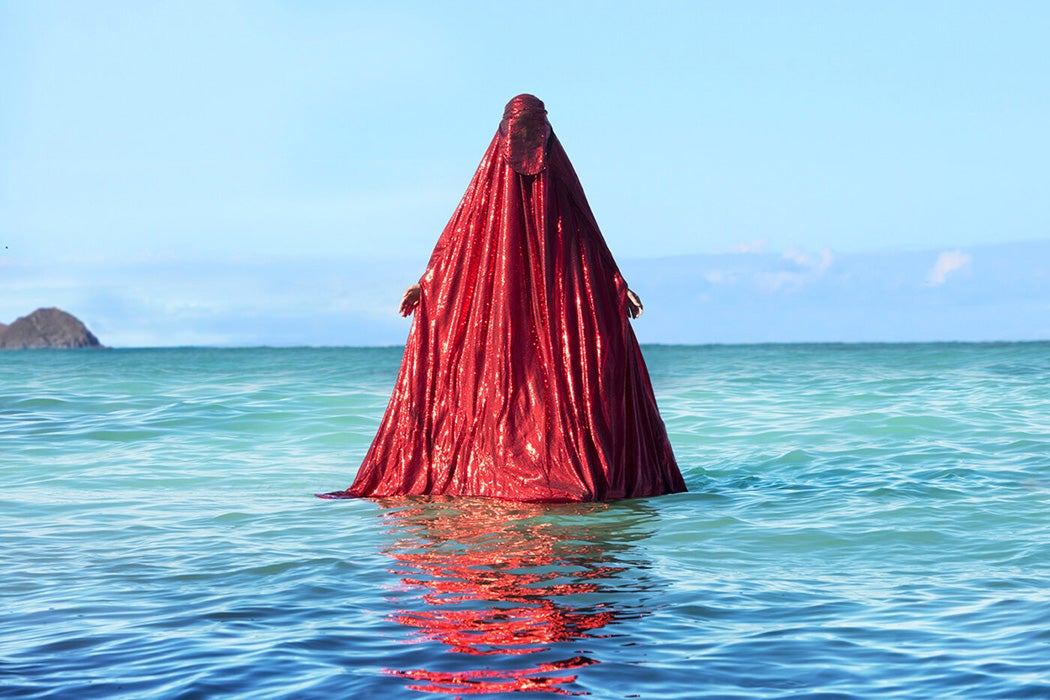 Anida Yoeu Ali, Water Birth, The Red Chador: Genesis I, 2019, Kaiona Beach, Oahu, Hawaii, archival inkjet print. Photo by Masahiro Sugano. Courtesy of the artist.