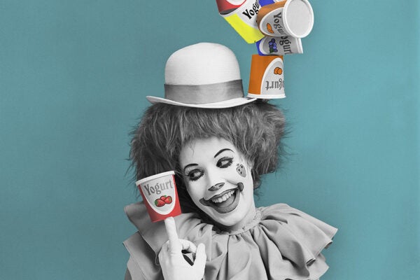 Woman in fancy dress costume balancing yogurt container on hat, smiling