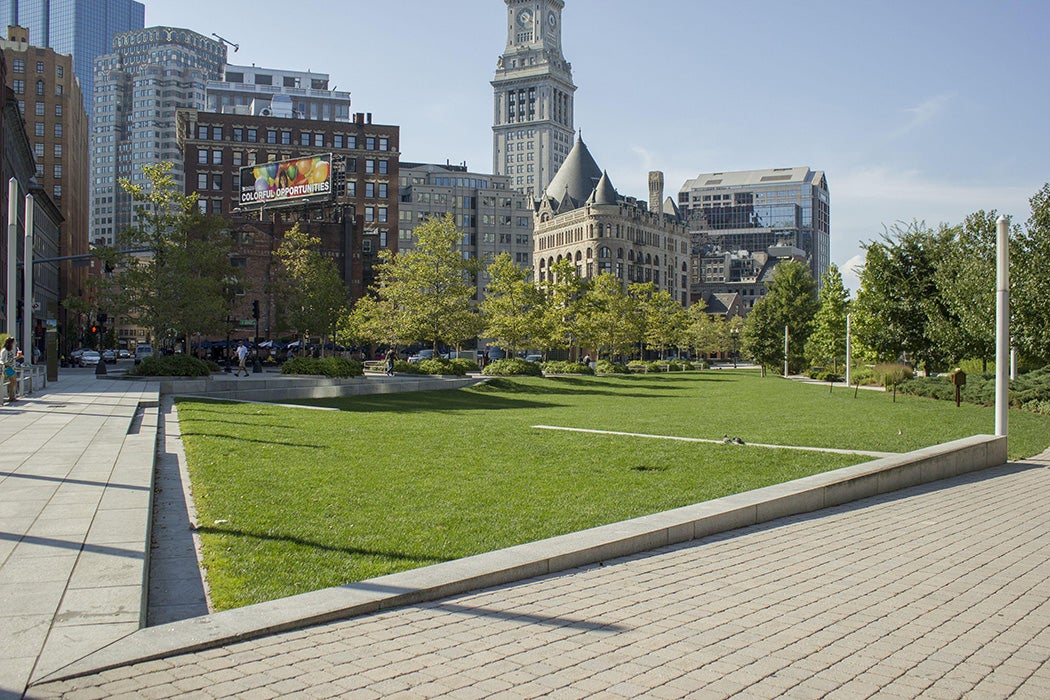 Wharf District Parks View of the edge of a large lawn adjacent to the Rowes Wharf patio area. The lawn is inset to allow for seating.