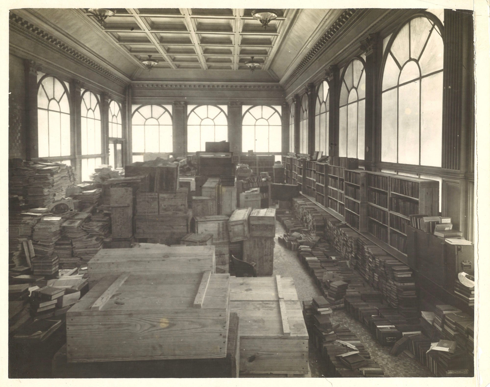 Ornate room lined with windows with wooden crates and books waiting to be packed or unpacked.
