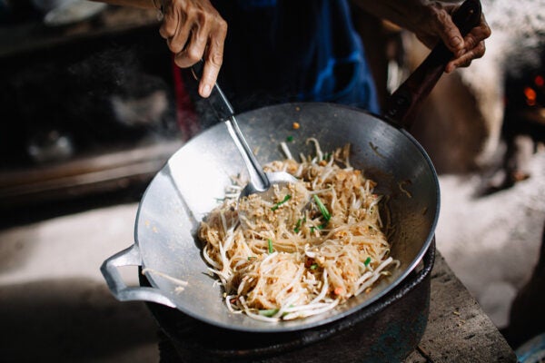 Cooking Thailand's most famous noodle dish, Pad thai in a small eatery in Kanchanaburi district. Phad thai consists of thin noodles lightly stir-fried with bean sprouts, sweet ground peanuts, and shrimp and is traditionally flash fried in a wok.